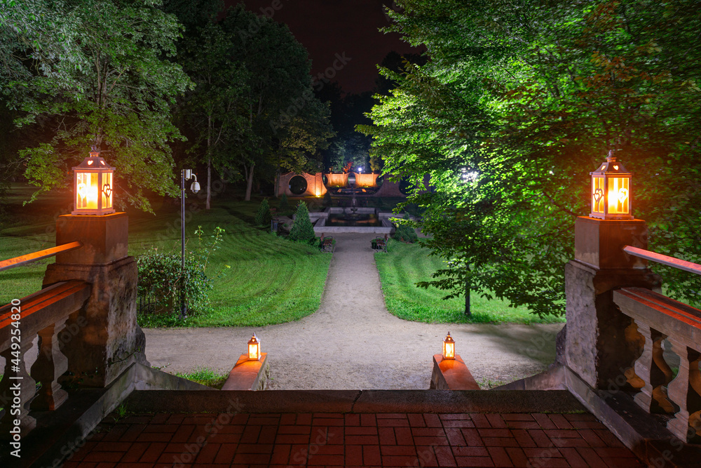 Park w mieście Iłowa w Polsce w nocnej scenerii. Ciemności rozświetlają lampiony ustawione na kamiennych schodach. - obrazy, fototapety, plakaty 