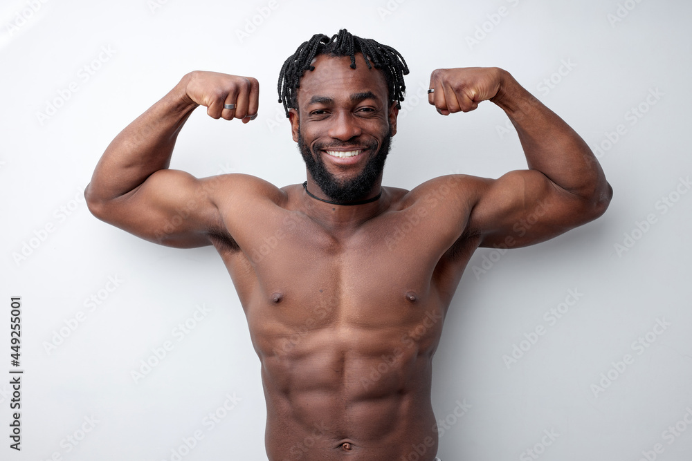 Fototapeta premium Afro American young fit athletic man showing biceps, isolated on white studio background, african black bodybuilder enjoy sport, show power and strength. Handsome bearded shirtless guy naked torso