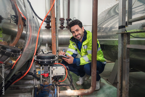 Caucasian engineer man in uniform checklist with clipboard sitting in steel pipeline and valves at processing factory © Mumemories