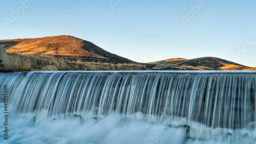 Photography water cascading over a diversion dam at creek in Colorado foothills, sunrise spr