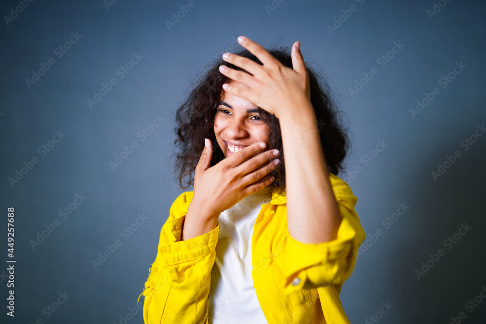 Portrait of happy emotional teenage girl with headphones hiding her face behind the hands in front of the camera. Wearing bright yellow cotton jacket and white shirt. Positive human concept Portrait of happy emotional teenage girl with headphones hiding her face behind the hands in front of the camera. Wearing bright yellow cotton jacket and white shirt. Positive human concept