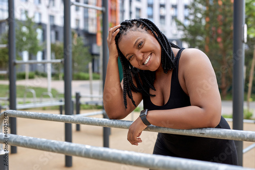 Optimistic african american lady in black sportive outfit taking a break after sport workout. Attractive black obese overweight woman having rest, sport in the morning outdoors. side view portrait