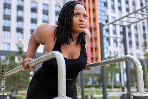 Confident overweight woman training on sports ground, looking at side, focused on sport workout, exercising alone. plus size woman in black sportive outfit. side view. copy space. weight loss