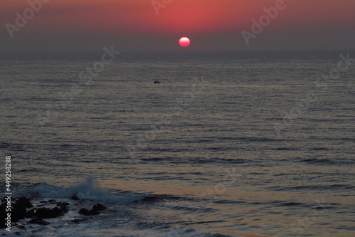 Sunrise over ocean with birds over sun and boat in foreground