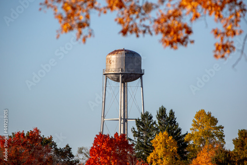 A vintage steel small town water tower standing in morning light and blue skies surrounded by fall color autumn trees_04 photo