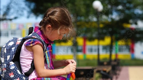 Little girl with a backpack and in a school uniform in the school yard plays pop it toy. Back to school, September 1. The pupil relaxes after lessons. Primary education, elementary class for student photo