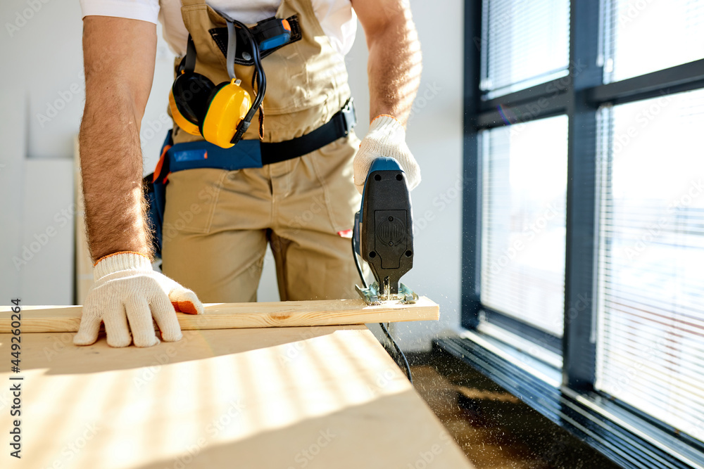 Close-up Carpenter Working On Wood With Electric Jigsaw In New House. Joinery Work On The Production And Renovation Of Wooden Furniture. Small Business Concept Close-up Carpenter Working On Wood With Electric Jigsaw In New House. Joinery Work On The Production And Renovation Of Wooden Furniture. Small Business Concept