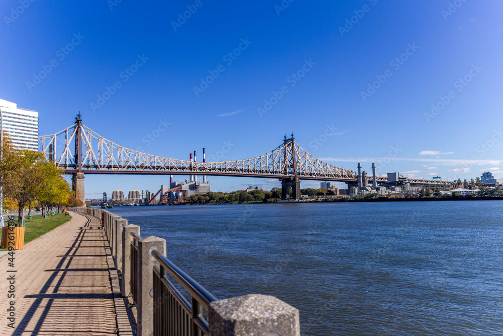 A picture of Ed Koch Queensboro Bridge in New York City, USA. In the picture one can see the East River, the Roosevelt island, Brooklyn and Domino Sugar Refinery and park