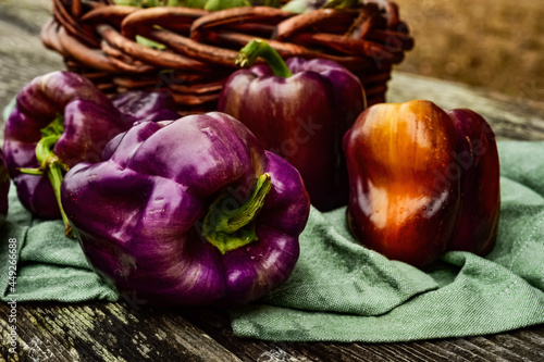 whole fresh purple bell peppers in food still life on rustic wood tabletop with green cloth and wicker basket