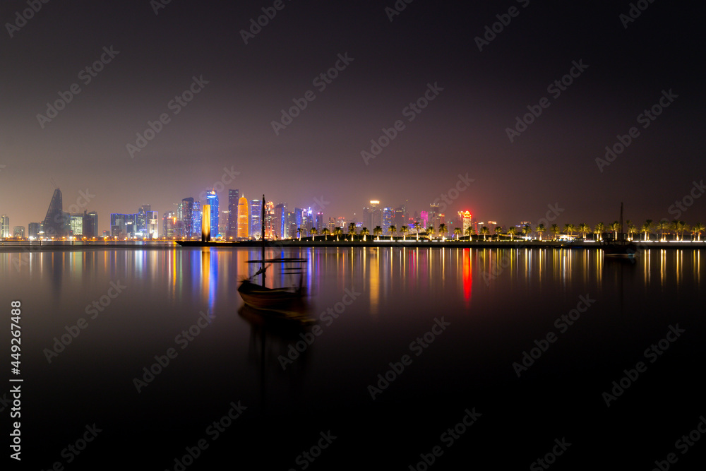 Illuminated skyline of Doha at night with traditional wooden boat in the foreground, Qatar, Middle East.
