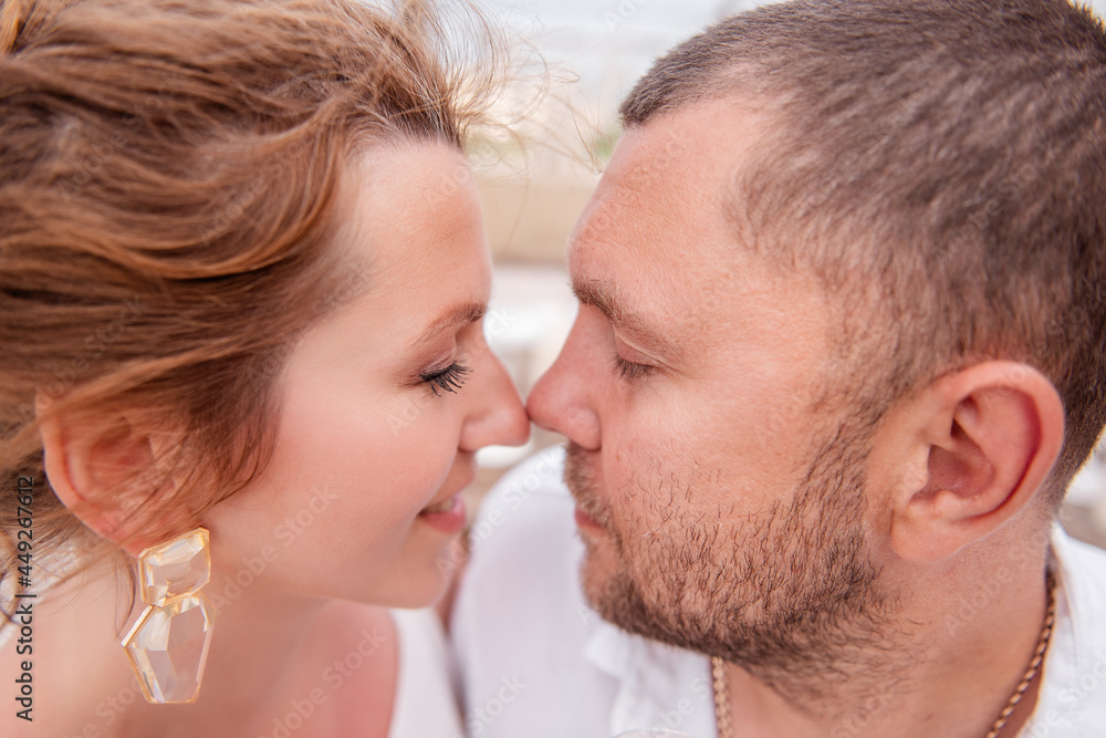 A very close-up portrait of a couple in love who looks at each other, touching nose to nose. The lovers in white laugh. Young woman with natural natural makeup, glass earrings. A man with a beard A very close-up portrait of a couple in love who looks at each other, touching nose to nose. The lovers in white laugh. Young woman with natural natural makeup, glass earrings. A man with a beard