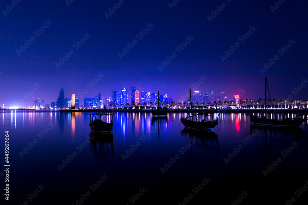 Illuminated skyline of Doha at night with traditional wooden boats in the foreground, Qatar, Middle East.