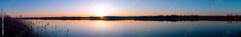 Panorama of the evening lake with a swan and the sun, colorful shades in the sky.