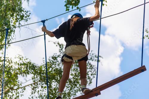 A girl on a tree climbs with a safety net.