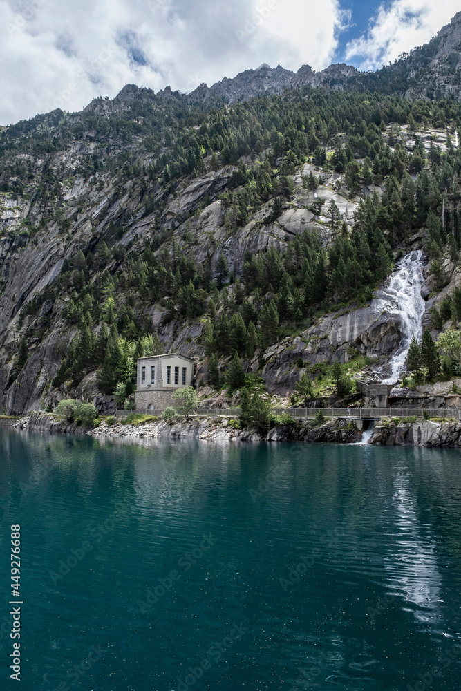 Cavallers reservoir between high mountains, a waterfall and a building of the hydroelectric power station, river Noguera de Tor in Alta Ribagorza