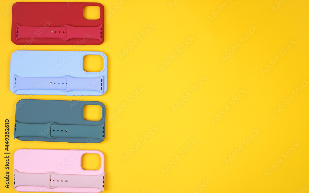 Colored silicone phone cases, complete with watch strap. Set. Up to date technology. Flat lay of diverse personal accessory laying on the yellow background. Space for text