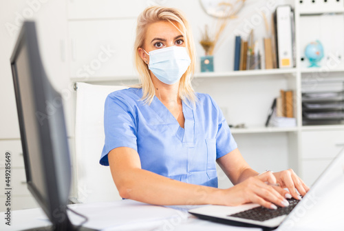 Medical female worker enters patient data into laptop