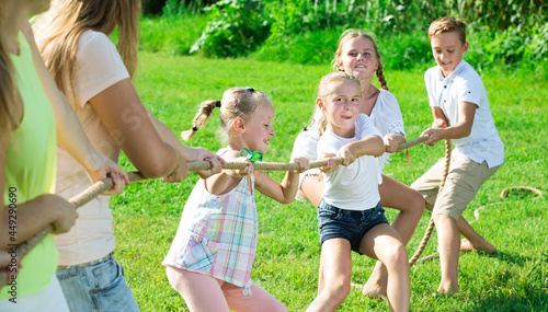 Glad kids with parents playing tug of war during joint outdoors games on sunny day