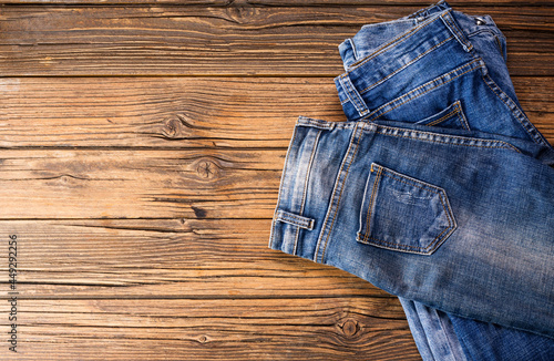 Two blue jeans resting on a dark brown wooden table. Modern fashion jeans - top view with space to copy text.