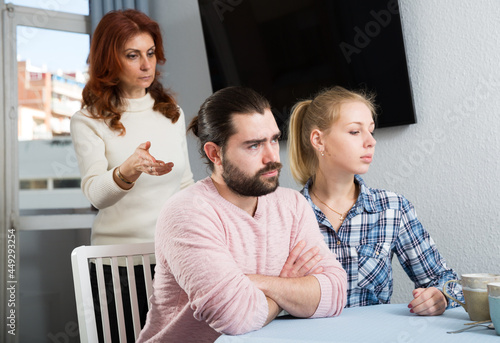 Upset mature woman talking with sad daughter and her boyfriend at home interior