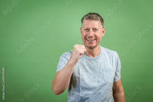 middle aged man with grey t-shirt and grey hair is posing in front of green background