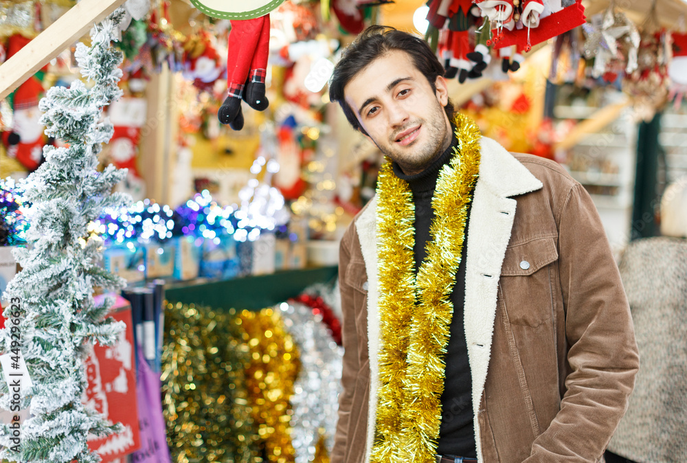 Smiling man with garland choosing decorations at Christmas market