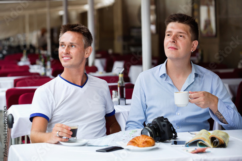 Positive couple of male tourists talking and drinking coffee