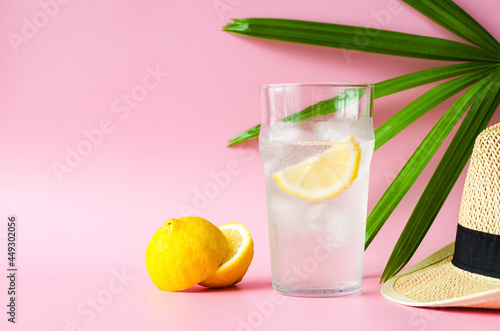 A glass of lemonade soda with hat and lady palm leaf on pink background. Summer drink concept. photo