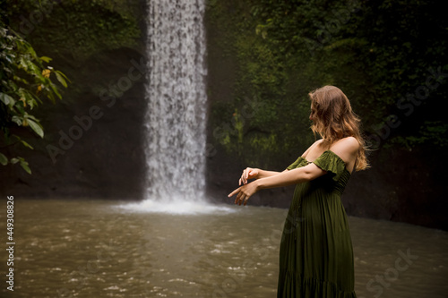 Portrait of Caucasian woman near the waterfall. Enjoy nature. Water splash. Young woman wearing green dress. Travel to Asia. Copy space. Tibumana waterfall  Bali