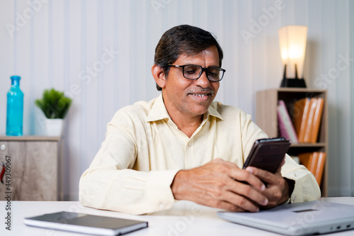 Middle aged businessman smiling while using mobile phone at office - concept of using social media, internet, checking mails and communication at workplace
