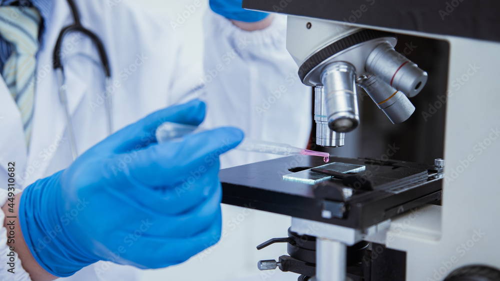medical or scientific researcher researching and experimenting Multi-colored solution, vial and microscope In the laboratory or in the laboratory by wearing blue gloves and white clothing completely. medical or scientific researcher researching and experimenting Multi-colored solution, vial and microscope In the laboratory or in the laboratory by wearing blue gloves and white clothing completely.