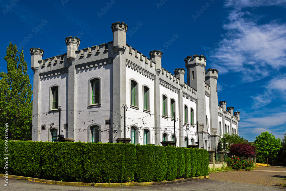 Old castle on top of a hill in the city of New Westminster BC, Canada. White castle surrounded by green trees and bushes against a blue cloudy sky