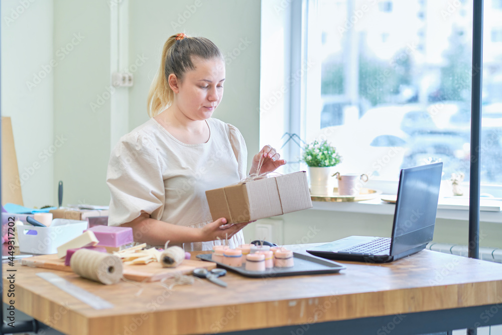 Small business owner. Portrait of mature woman standing at her shop behind the laptop and smiling. female online store seller entrepreneur packing package post shipping box preparing delivery parcel. Small business owner. Portrait of mature woman standing at her shop behind the laptop and smiling. female online store seller entrepreneur packing package post shipping box preparing delivery parcel.