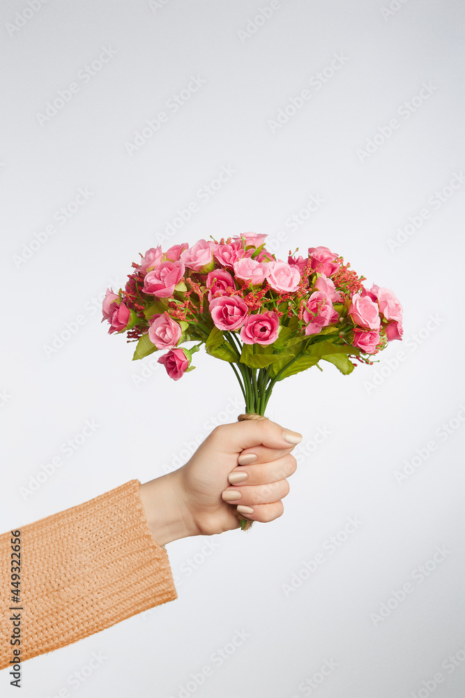 Cropped shot of female hand holding graceful bouquet of tender pink roses with ornamental herbs. Photo of flowers for interior decorating is made on the gray background. 