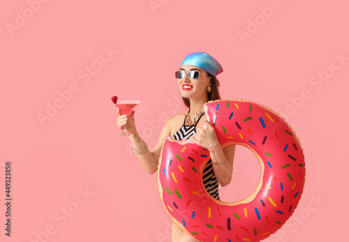 Beautiful young woman with cocktail and swimming ring on color background photo