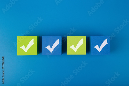 Creative flat lay with four checkmarks on blue and yellow toy cubes with in the middle of blue background. Concept of questionary, checklist, to do list, planning or business plans