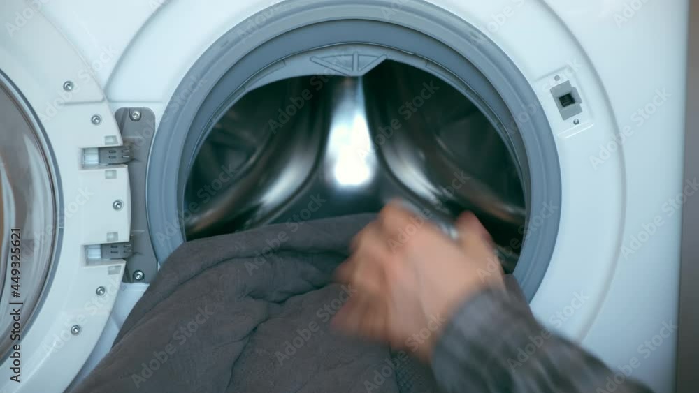 Man's hands loading the washing machine with bedspread, laundry at home. Man is doing his laundry and closing washing machine. Everyday life, housework of young man. Man's hands loading the washing machine with bedspread, laundry at home. Man is doing his laundry and closing washing machine. Everyday life, housework of young man.