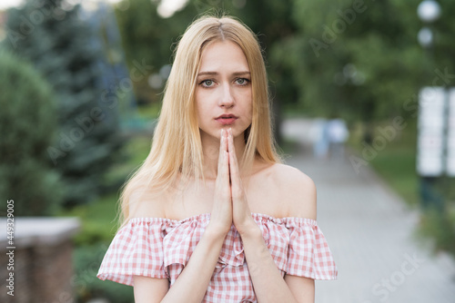 Portrait of a young and attractive caucasian blonde girl who showing a prayer gesture