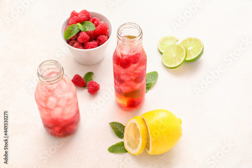 Bottles of delicious lemonade, bowl of raspberry and sliced lemon on light background