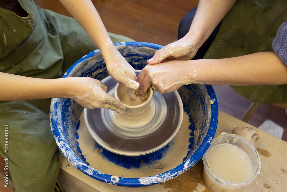 Close-up of a potter's hands and a child's hand with an item on a potter's wheel. Working with clay. Clay workshop. Craft training. Close-up of a potter's hands and a child's hand with an item on a potter's wheel. Working with clay. Clay workshop. Craft training.