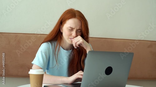 Medium shot portrait of serious attractive young woman student working on project using laptop in cozy cafe. Thinking Caucasian redhead female freelnacer working on laptop, coffee cup on table. photo