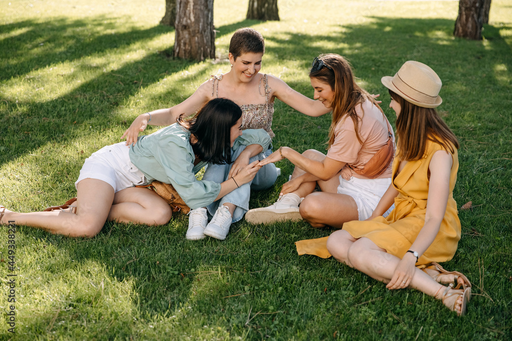 Group of young women sitting on grass outdoors in a park, chatting and smiling.