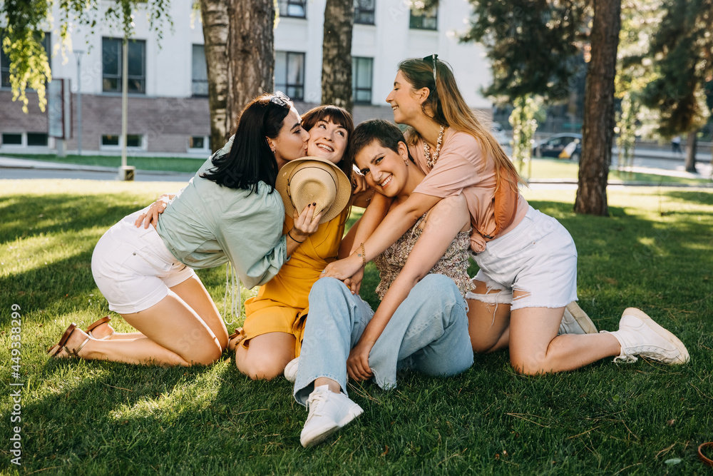 Group of four women sitting in a park on green grass, hugging and laughing. Group of four women sitting in a park on green grass, hugging and laughing.