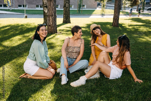Group of four friends sitting in a park on green grass, having good time.
