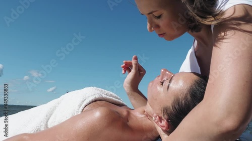 Close up. Female massage therapist doing neck massage to brunette girl on the beach during summer, massage procedure. Young woman enjoying massage outside. Healthy lifestyle and body care concept