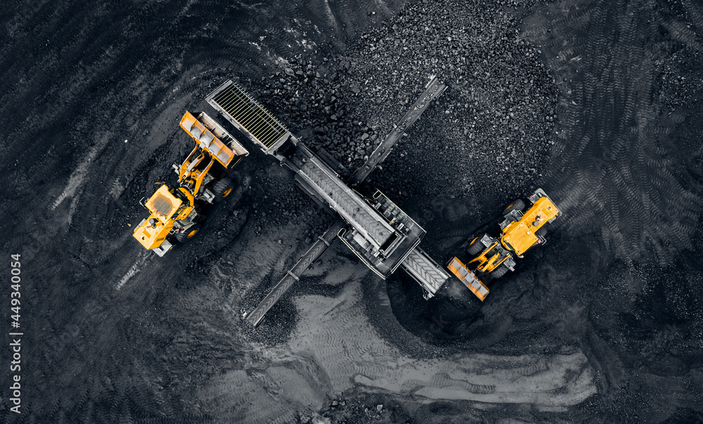Yellow Excavator loads anthracite for crushing into coal crusher in open mine, aerial top view Yellow Excavator loads anthracite for crushing into coal crusher in open mine, aerial top view