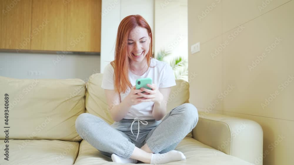 Portrait excited young woman winner screaming yes rejoicing success looking at cellphone. Happy overjoyed girl holding mobile phone celebrate good news surprise bid win app victory sit on sofa at home Portrait excited young woman winner screaming yes rejoicing success looking at cellphone. Happy overjoyed girl holding mobile phone celebrate good news surprise bid win app victory sit on sofa at home