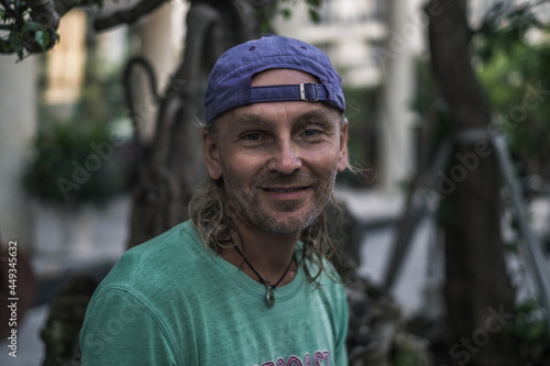 Close up portrait of smiling elderly man with long grey hair wearing green t-shirt and cap. Homeless person. Hippy style.