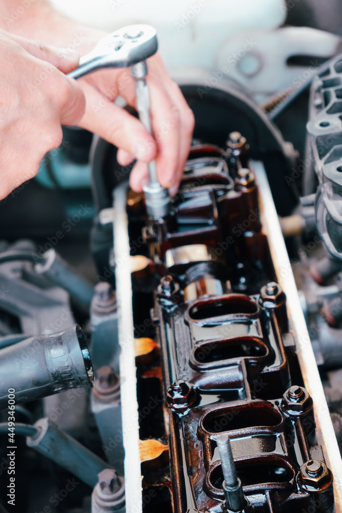 Obraz premium Car service. An auto mechanic repairs a car engine. Internal combustion engine valve adjustment. Close-up on the engine and hands with the tool.