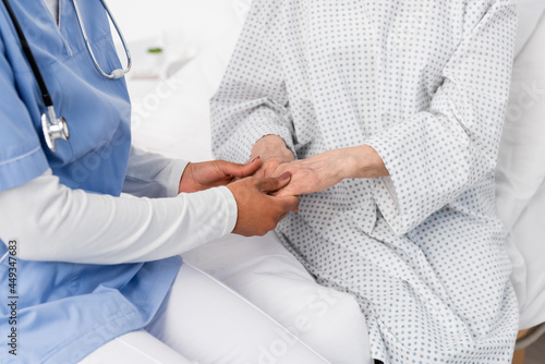 Cropped view of african american nurse holding hands of senior patient in gown